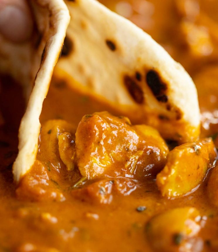 close up shot of flatbread scooping up curry in pan