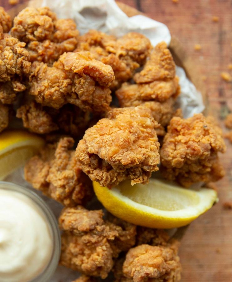 overhead shot of chicken stacked on wooden board served with pot of mayo and lemon wedge