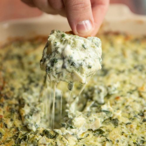 Ritz cracker scooping out dip out of dish with cheese pull