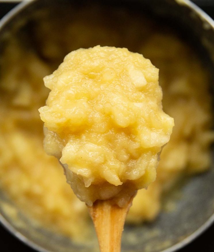 overhead shot of apple sauce on wooden spoon over pot