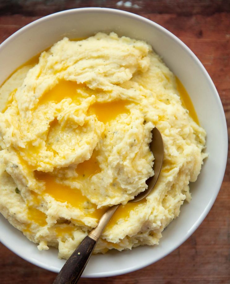 overhead shot of mashed potatoes in large white bowl with gold spoon digging in