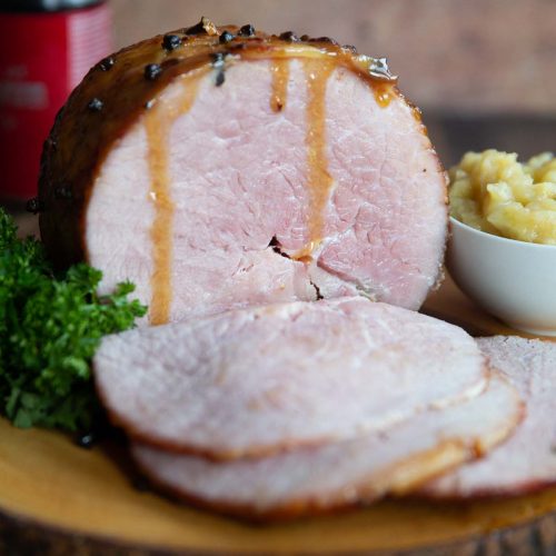 ham on wooden board next to parsley and apple sauce