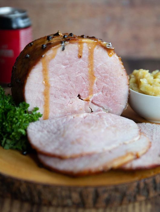 ham on wooden board next to parsley and apple sauce