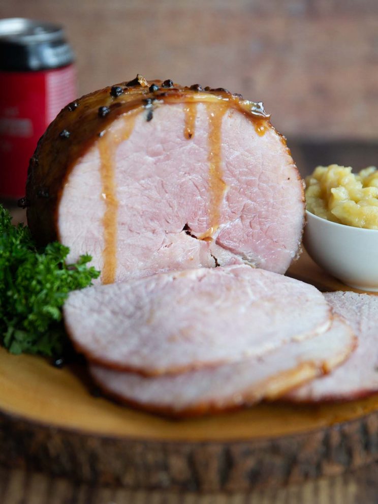 ham on wooden board next to parsley and apple sauce