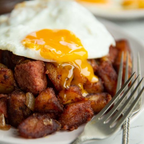 fried egg on corned beef hash with yolk dripping down on white plate