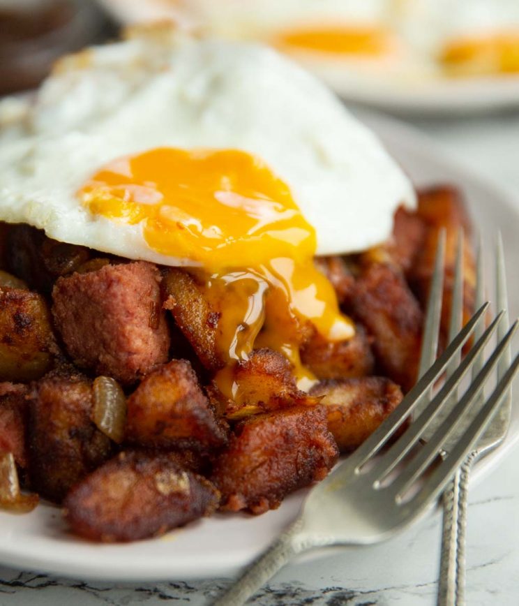 fried egg on corned beef hash with yolk dripping down on white plate