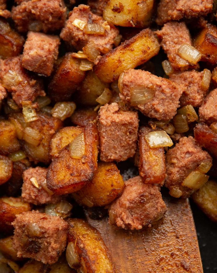 over head shot of corned beef hash in skillet with wooden spoon digging in