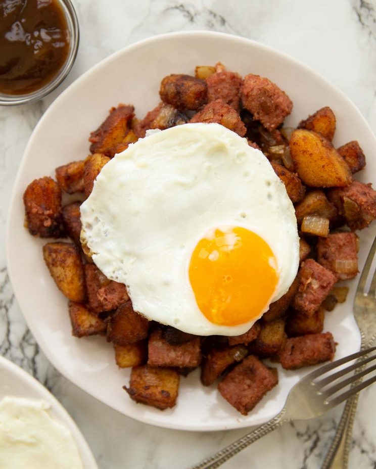 overhead shot of fried egg on corned beef hash on white plate with marble background