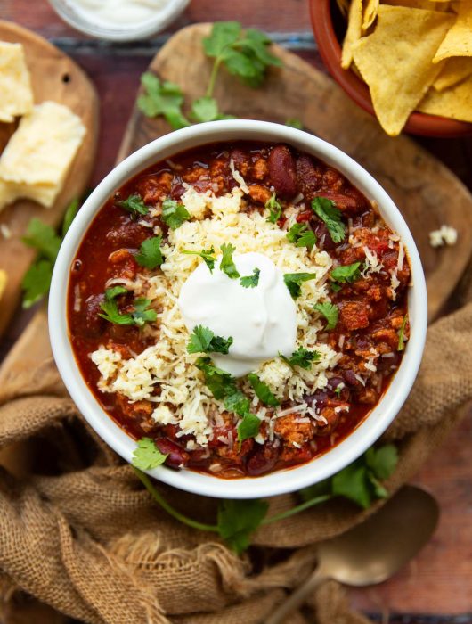 overhead shot of chili in white bowl with sour cream, cheese and cilantro