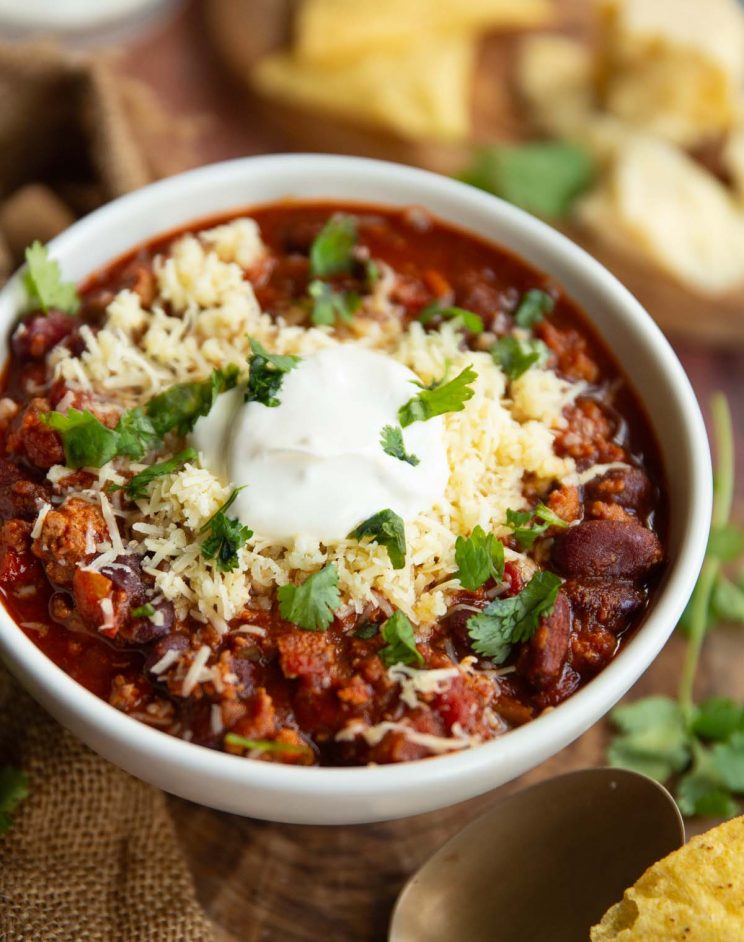close-up of chili in white bowl with blurred garnish in the background