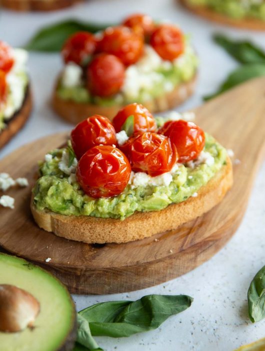tomato avocado toast on wooden board surrounded by toast and garnish
