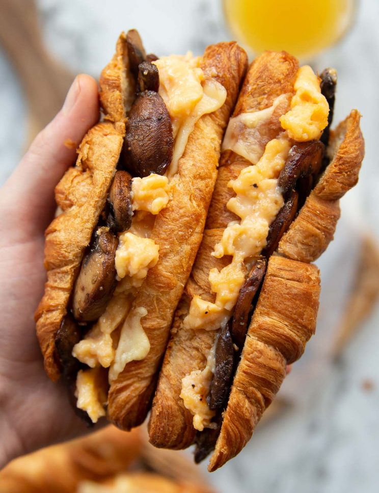 overhead shot of hand holding two croissants above chopping board