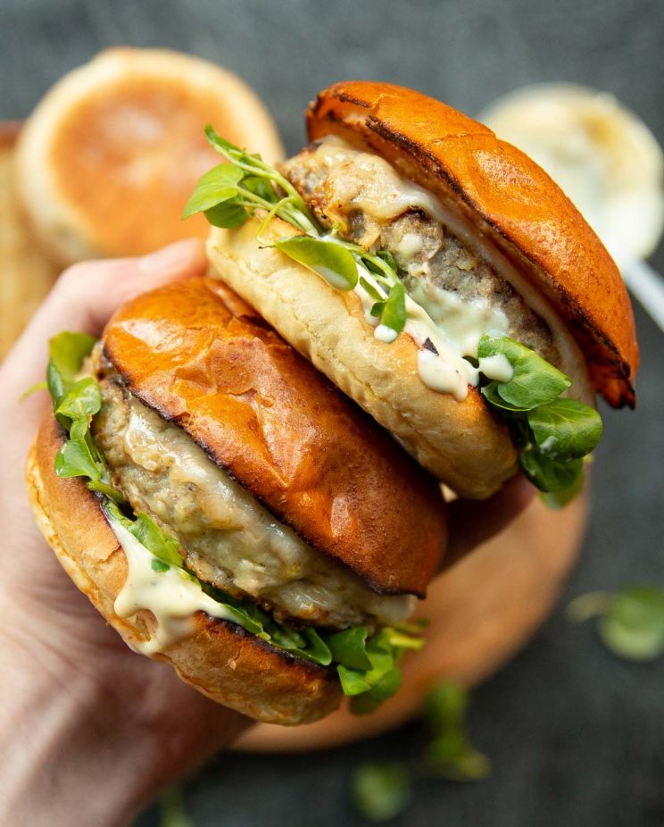 overhead shot of hand holding two burgers above ingredients