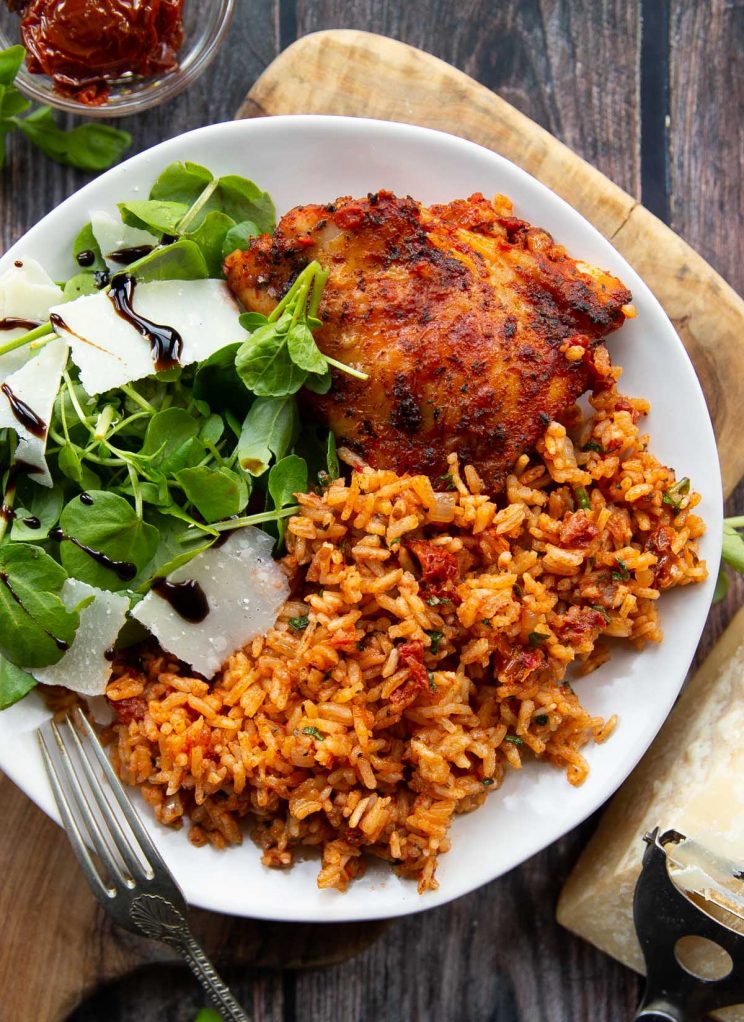overhead shot of chicken served with rice on small white plate with salad
