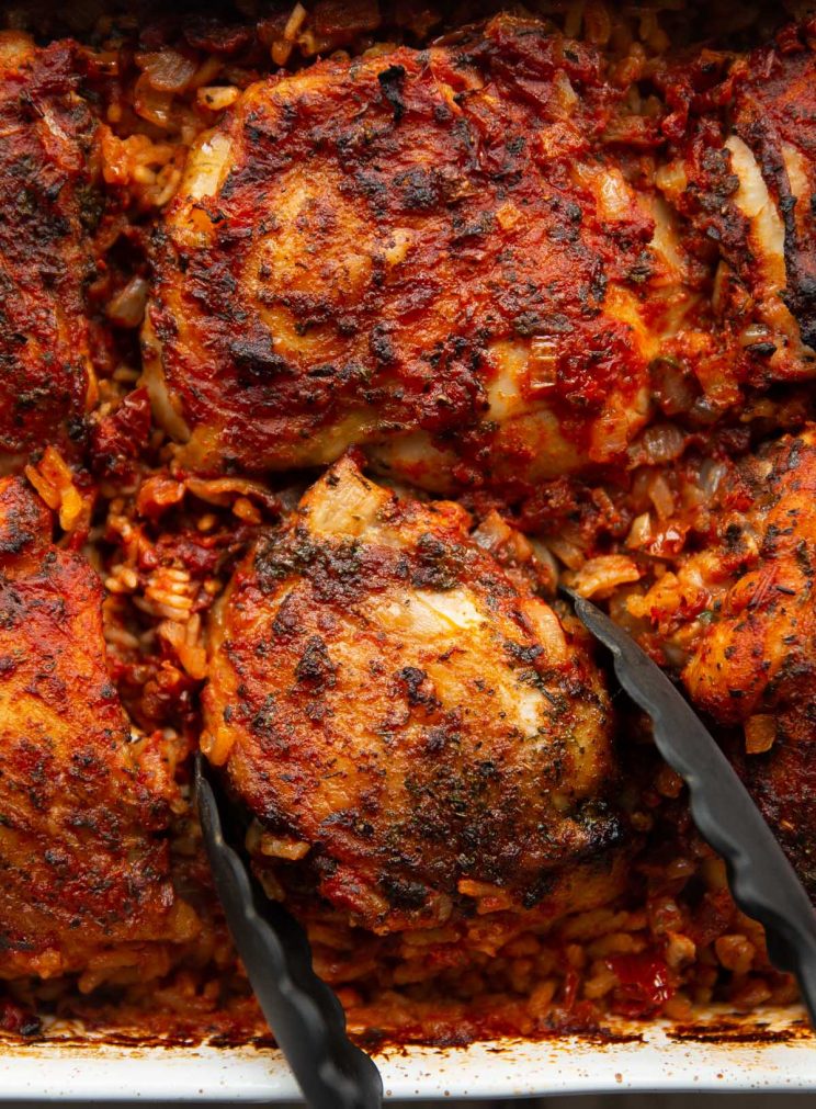 overhead shot of chicken and rice freshout the oven with tongs grabbing chicken