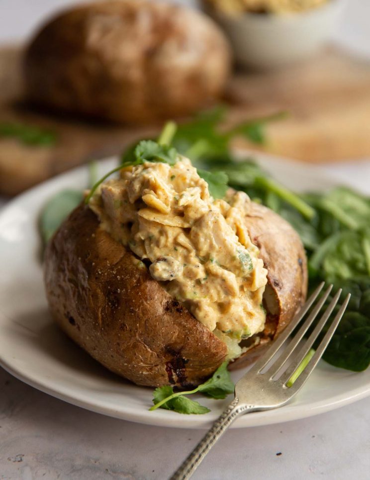 coronation chicken served in a baked potato on white plate with spinach
