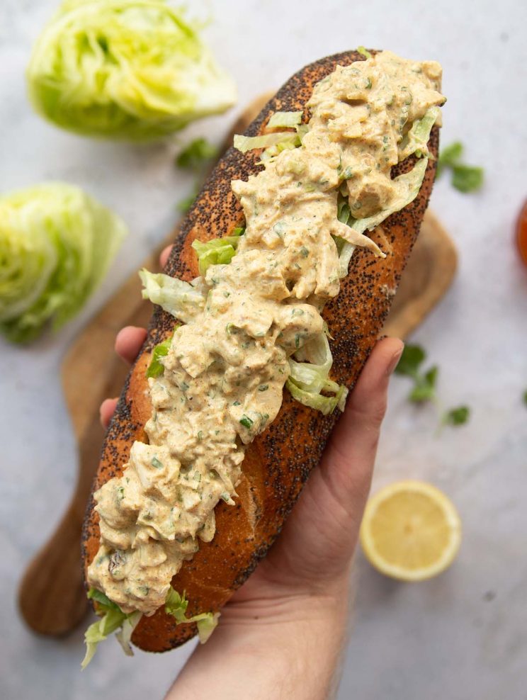 overhead shot of hand holding baguette filled with coronation chicken above garnish