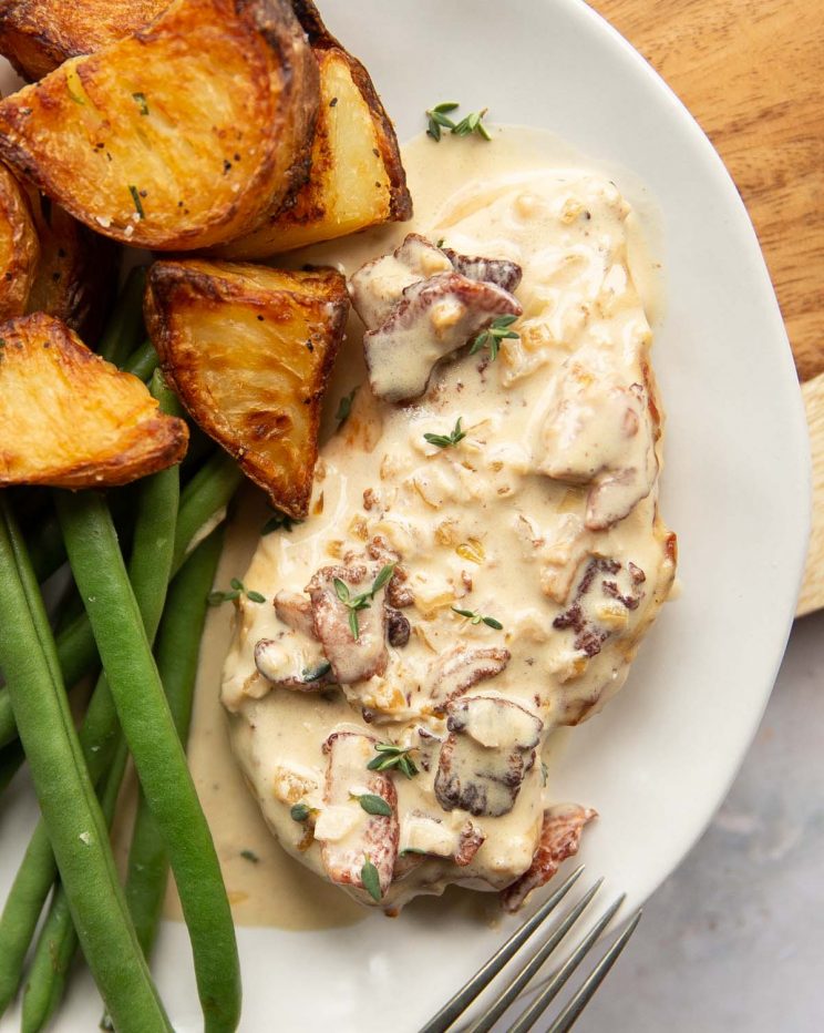 overhead shot of chicken breast on white plate served with roast potatoes and green beans