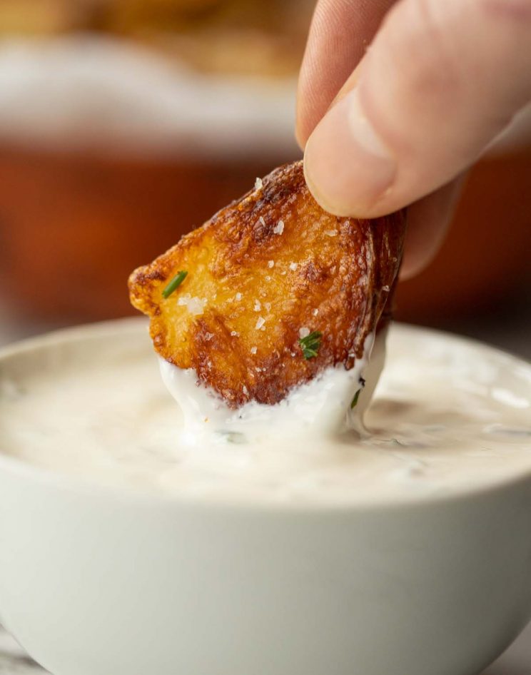 close up shot of potatoes being dunked into pot of creamy dip