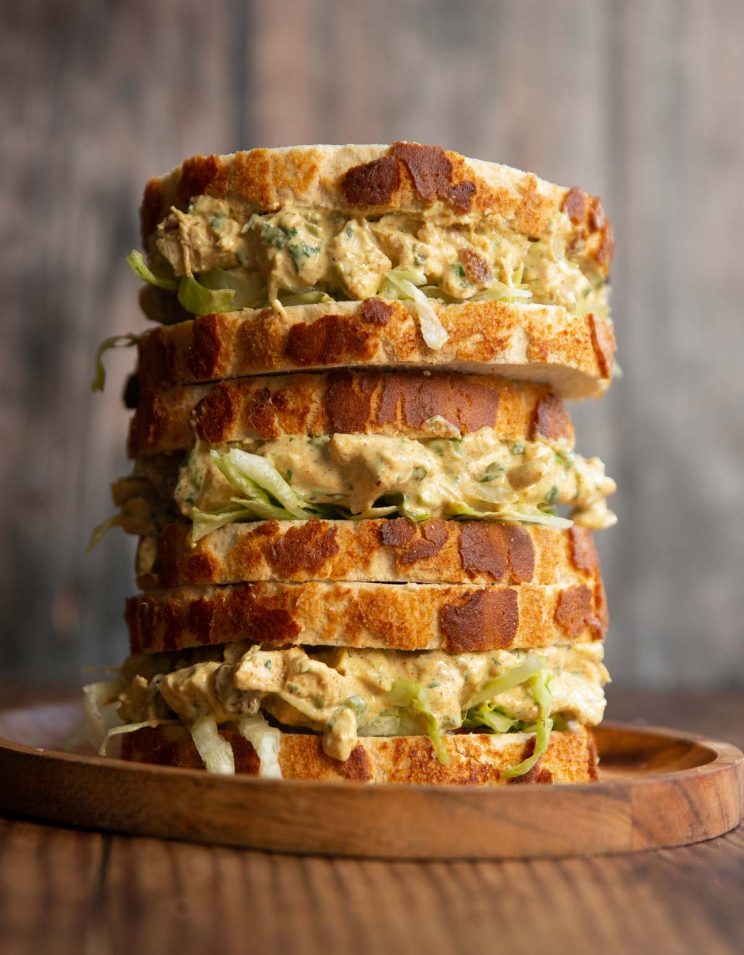3 coronation chicken sandwiches stacked on each other on small wooden board
