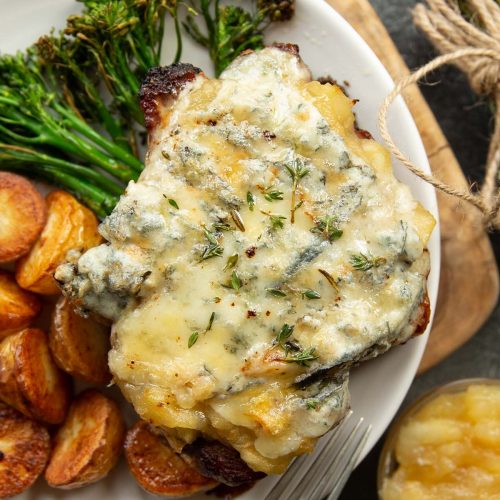 overhead shot of pork chop on white plate served with potatoes and broccolini