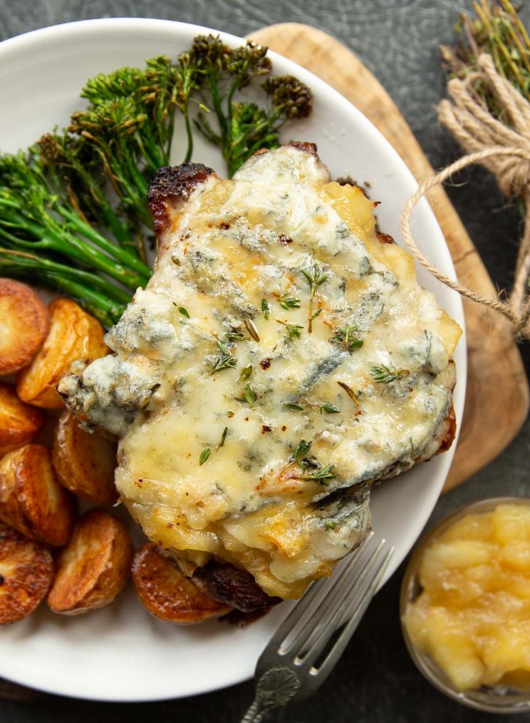 overhead shot of pork chop on white plate served with potatoes and broccolini