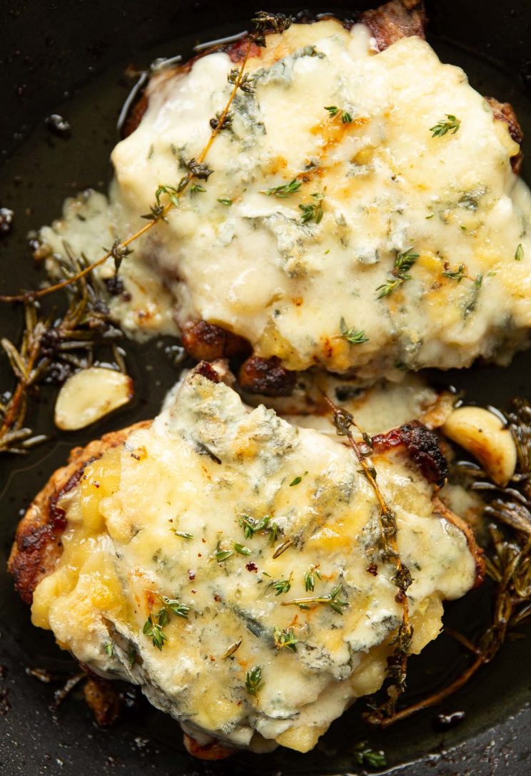 overhead shot of pork chops with applesauce and melted blue cheese in pan