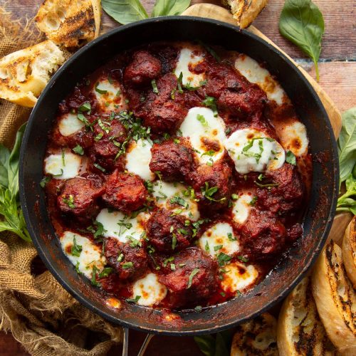 overhead shot of meatballs in skillet surrounded by fresh basil and garlic bread