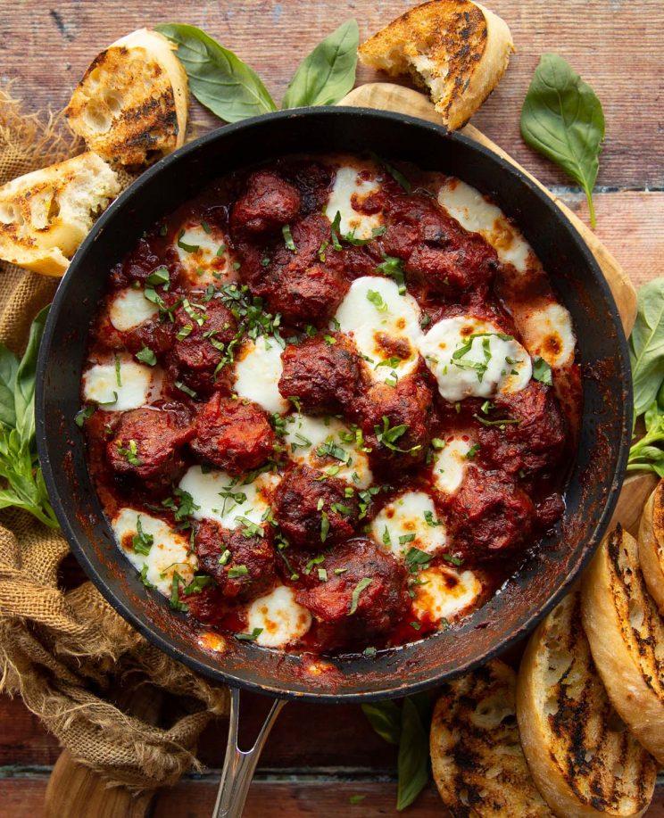 overhead shot of meatballs in skillet surrounded by fresh basil and garlic bread