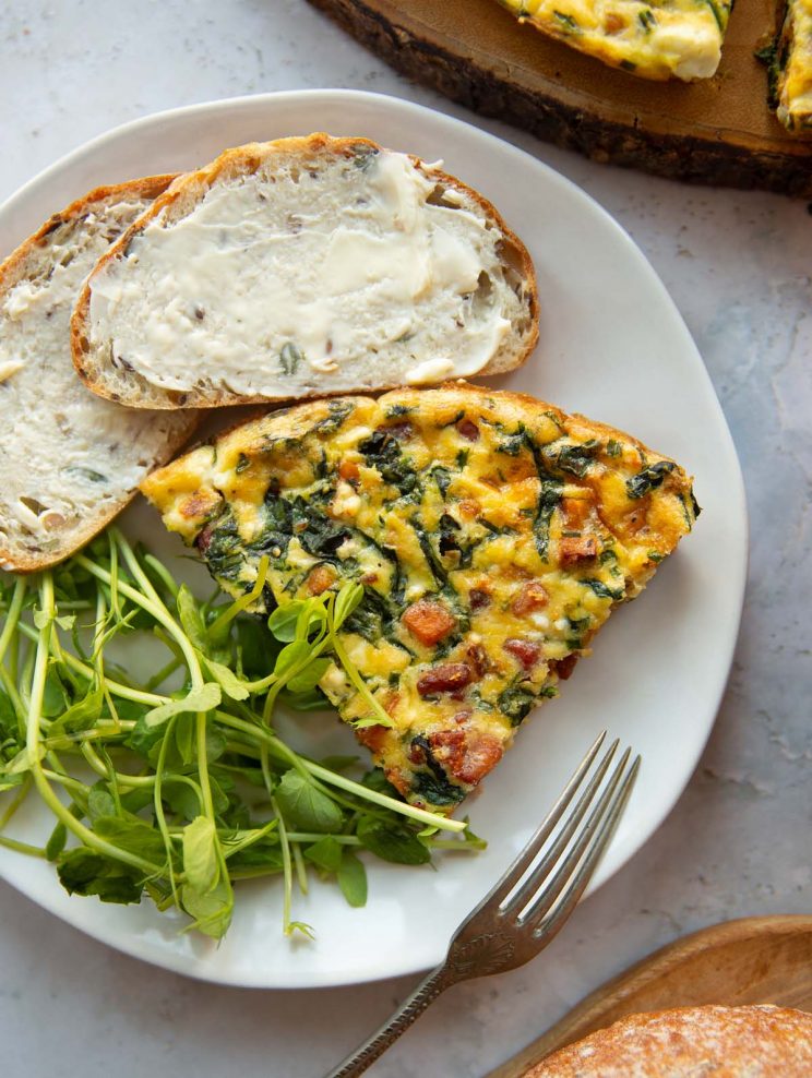 overhead shot of slice of frittata on white plate with peashoots and buttered bread