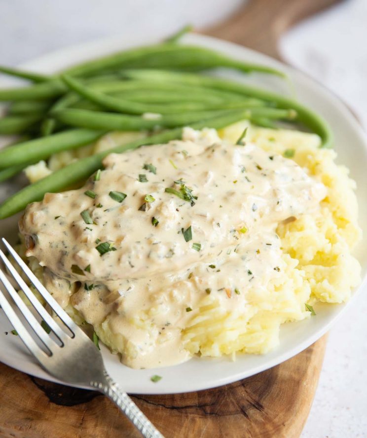 chicken on mashed potato served with green beans on white plate