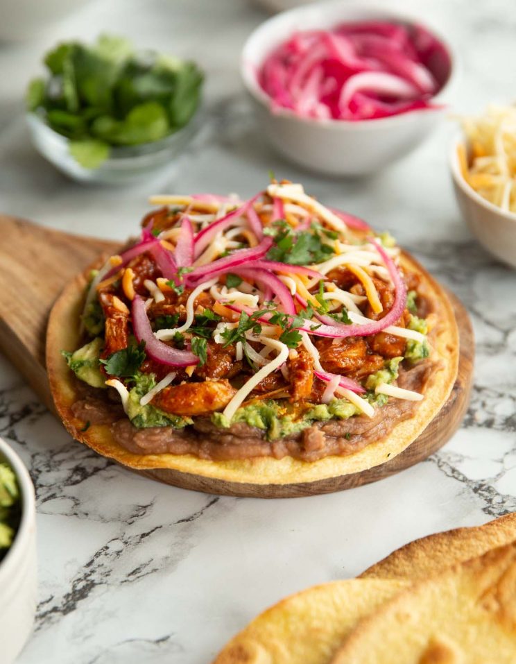 close up shot of tostada on small wooden board surrounded by toppings