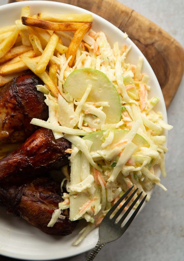 overhead shot of apple slaw, chicken drum sticks and fries on small white plate