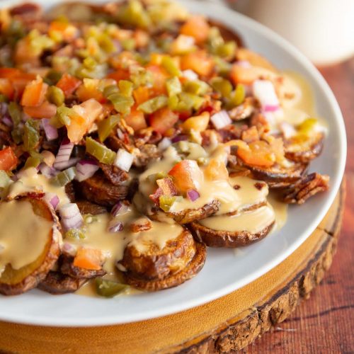 potato nachos on large white plate with can of Guinness and pot of cheese sauce blurred in background