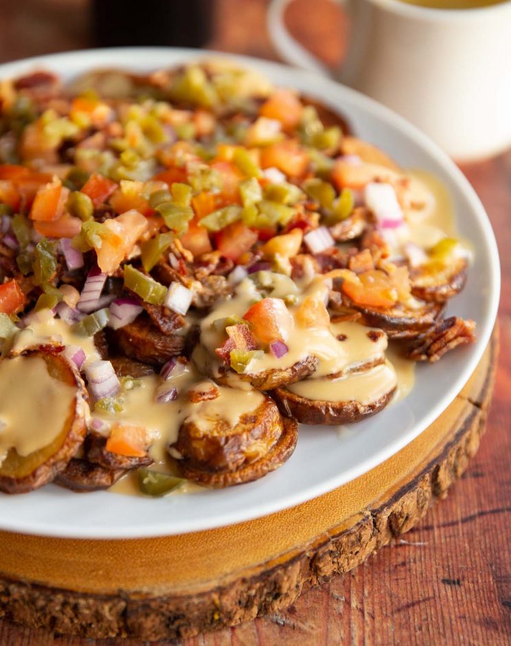 potato nachos on large white plate with can of Guinness and pot of cheese sauce blurred in background