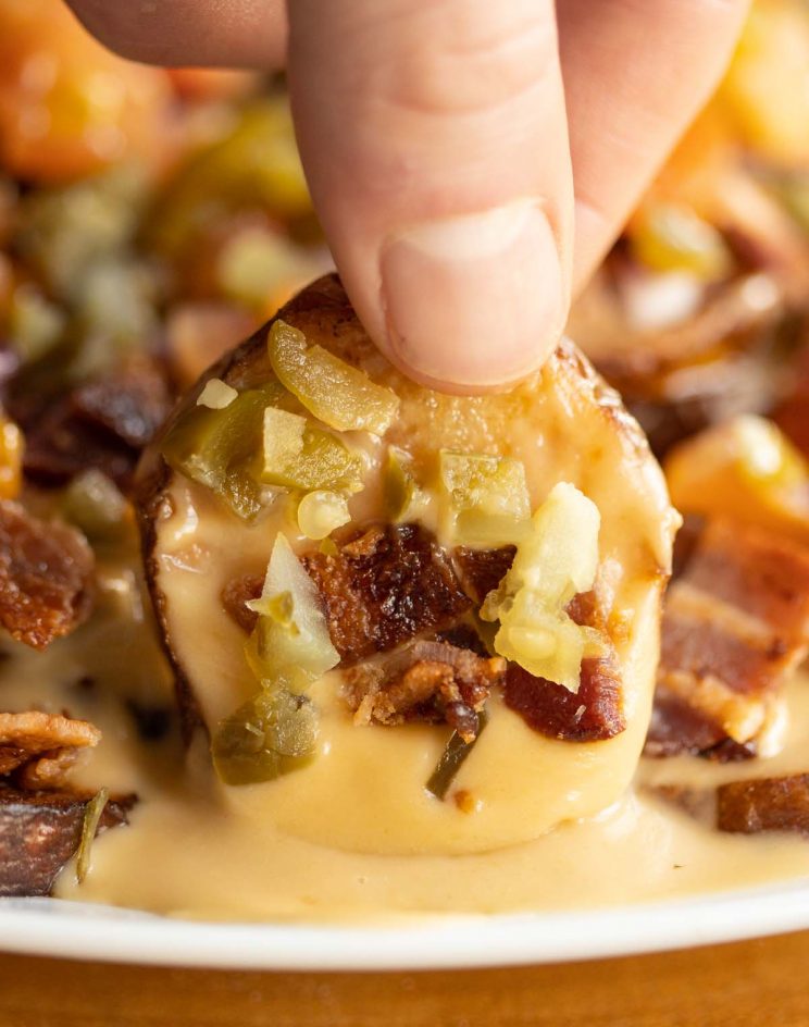 close up shot of fingers lifting up nacho off of white plate