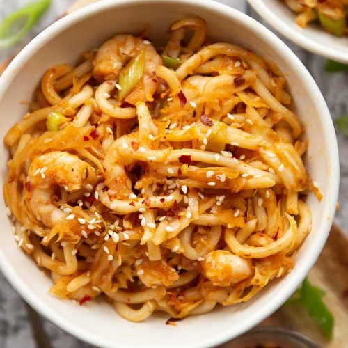 overhead shot of noodles in small white bowl garnished with chilli flakes and sesame seeds