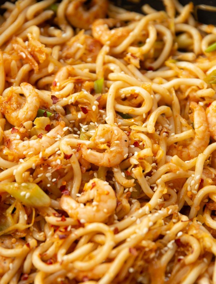 closeup shot of prawn noodles in skillet garnished with sesame seeds and chilli flakes