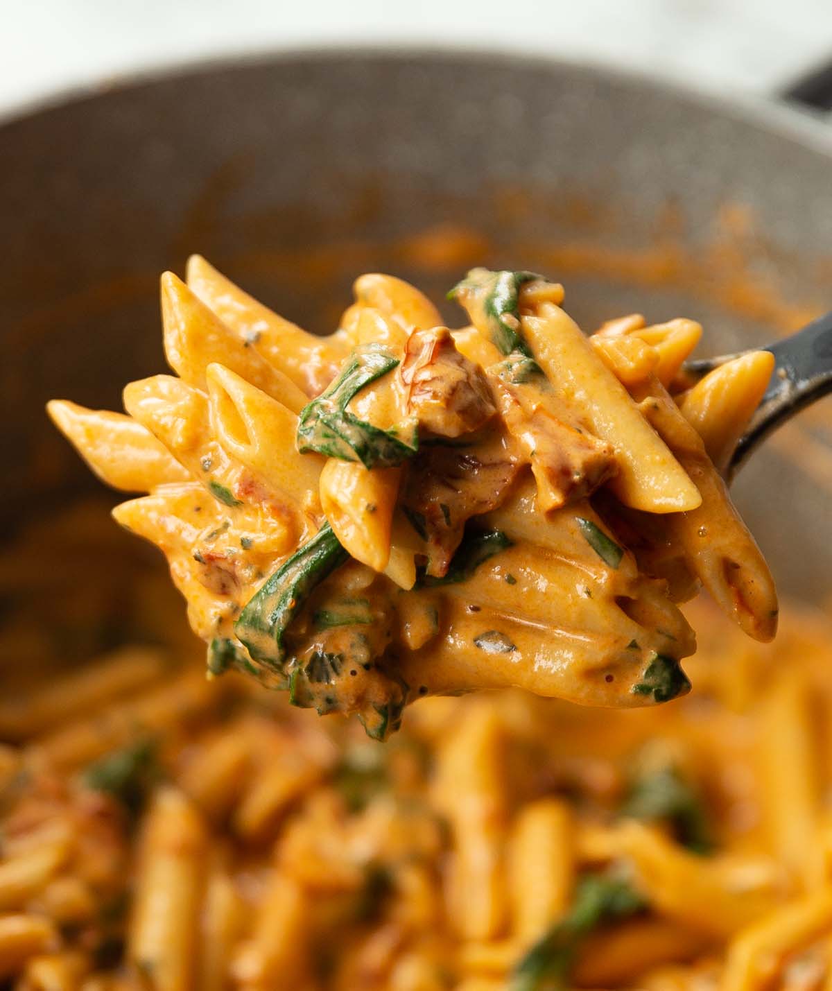 close up shot of pasta on black serving spoon above pot