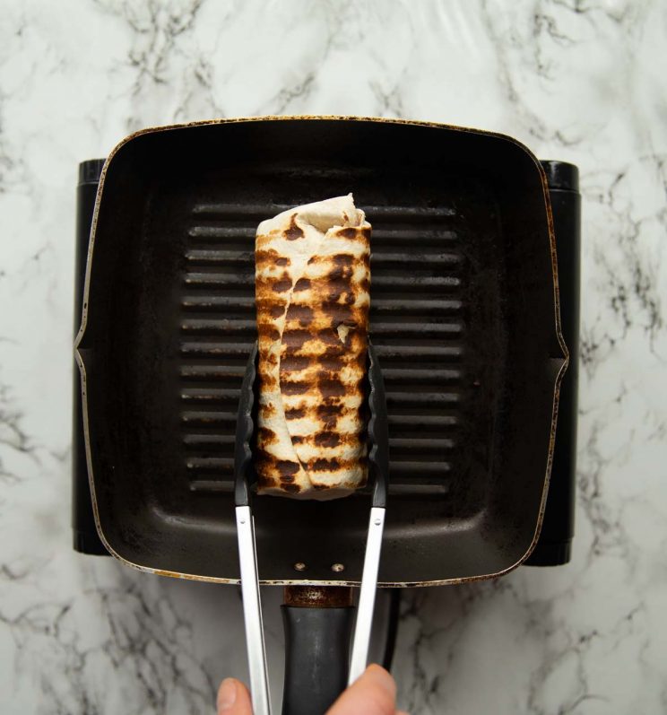 overhead shot of tongs holding toasted wrap on griddle pan
