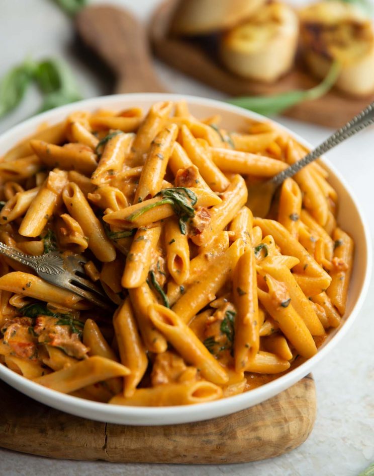 tomato spinach pasta served in large white bowl with garlic bread and basil blurred in background