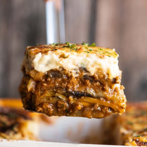 close up shot of metal spatula scooping moussaka out of dish