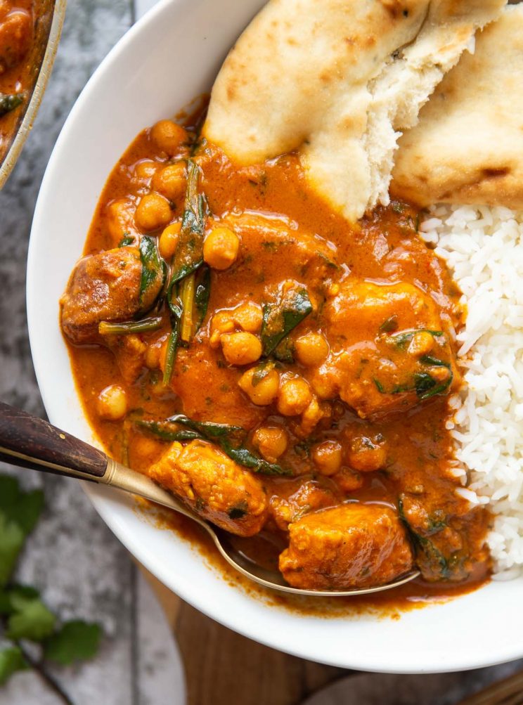 overhead close up shot of curry in white bowl with naan and rice with gold spoon