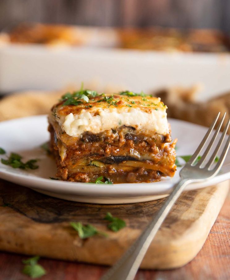 moussaka on small white plate with silver fork garnished with fresh parsley