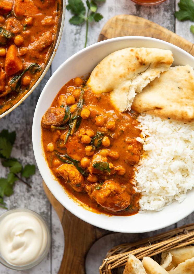 overhead shot of curry served in large white bowl with rice and naan