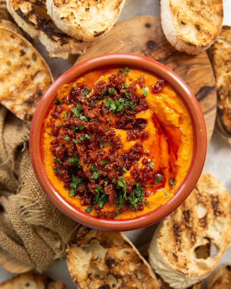 overhead shot of dip in small red bowl surrounded by toasted ciabatta