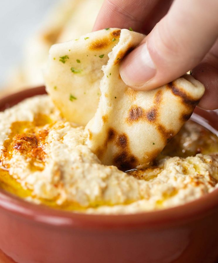 hand dunking flatbread into small pot of hummus