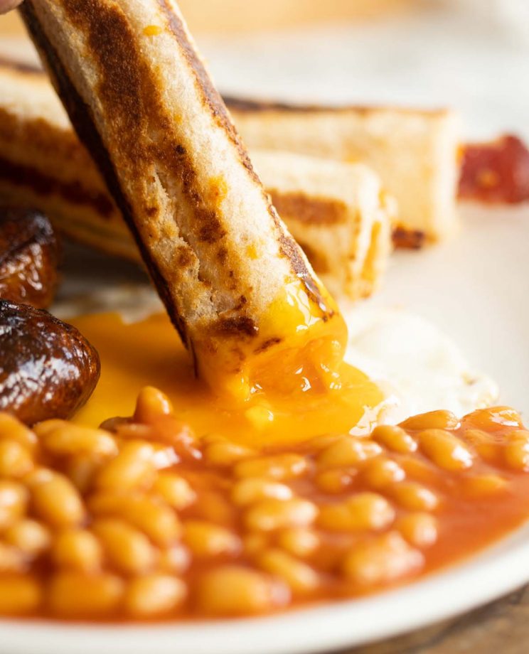 close up shot of dunking a grilled cheese roll up into a sunny side up egg