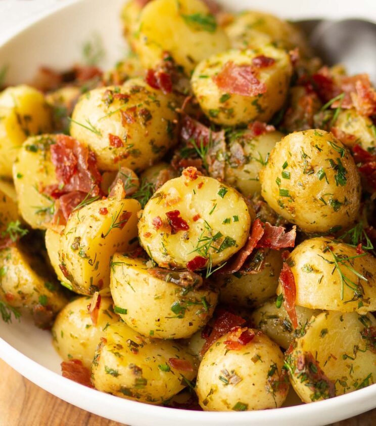 herbed potato salad served in white bowl with 2 silver spoon blurred in background