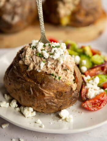 tuna baked potato on white plate with silver fork digging in next to side salad